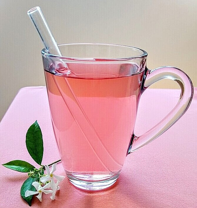 ToMA glas straw in glacier clear in a clear glass mug of cherry hibiscus tea on pink linen tablecloth with jasmine bloom.