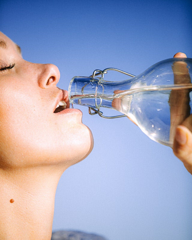 Photo of woman drinking from glass water bottle by Arnie Watkins of Pexels.
